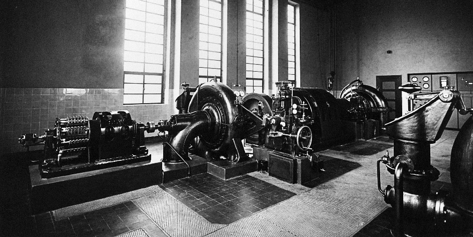 Historische Industrieanlage mit mehreren großen Maschinen und Fenstern im Hintergrund. Schwarz-Weiß-Foto.