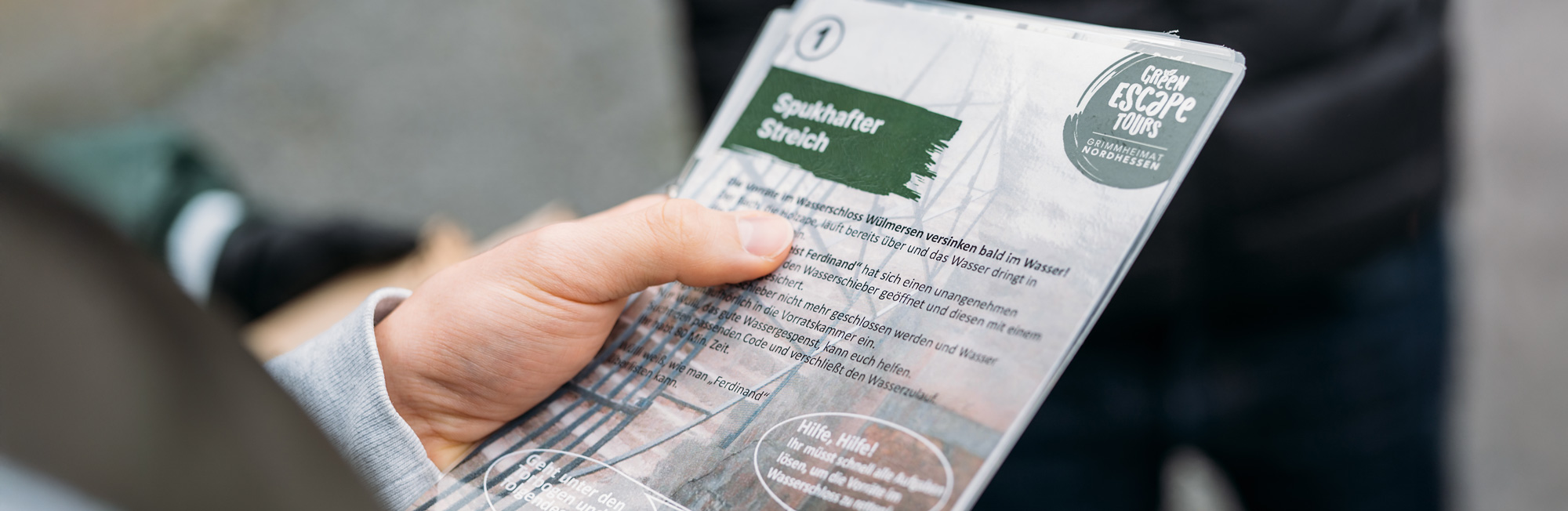 Hand hält eine Informationsbroschüre über eine geführte Tour mit dem Titel „Spukhafter Streich“.