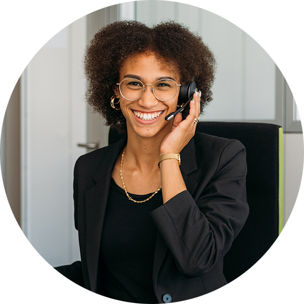Lächelnde Frau mit Locken und Headset, sitzt am Schreibtisch in einem modernen Büro.