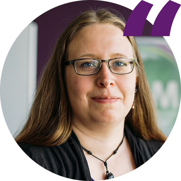 Porträt einer Person mit langen Haaren und Brille, lächelnd, vor lila Hintergrund, Quote-Symbol oben rechts.