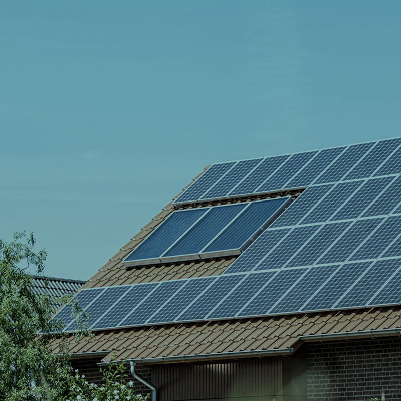 Solaranlage auf einem Dach, mit mehreren Solarpanelen und einem Dachfenster unter klarem Himmel.