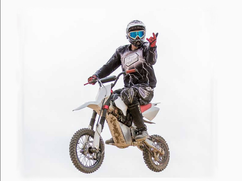 Motorradfahrer in Schutzkleidung, auf einem Dirtbike, zeigt ein Zeichen mit der Hand vor neutralem Hintergrund.