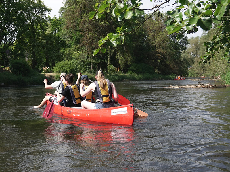 Gruppenausflug mit mehreren Personen im roten Kanu auf einem ruhigen Fluss, umgeben von grüner Natur.