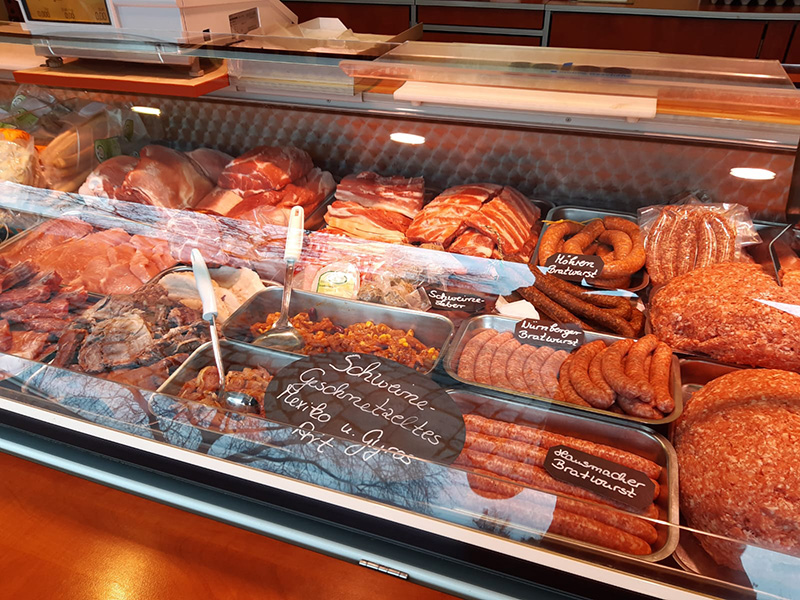 Theke mit verschiedenen Fleischsorten, Wurstwaren und Aufschnitt in einem Metzgerei-Geschäft.