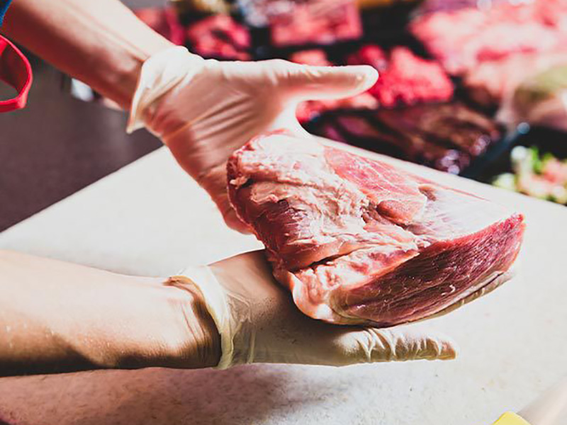 Eine Hand hält ein großes Stück rohes Fleisch auf einer Arbeitsfläche in einem Fleischgeschäft.