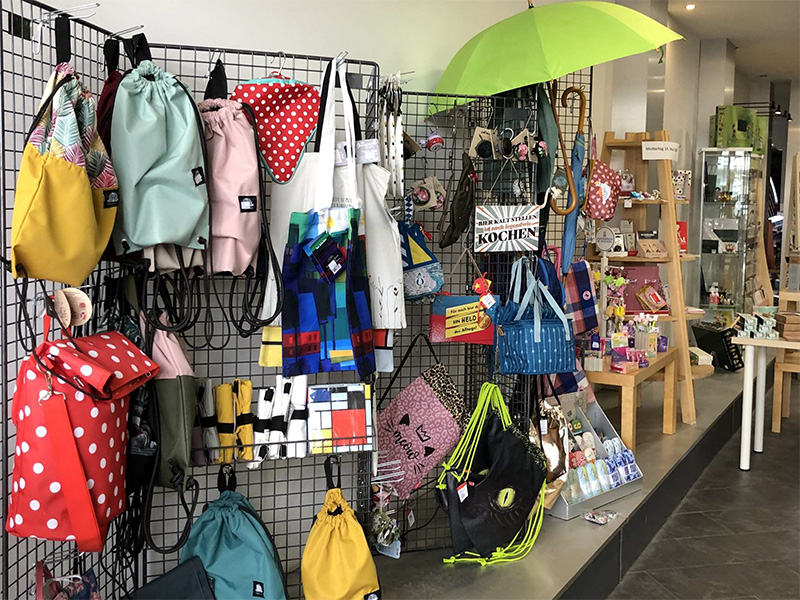 Verschiedene Taschen und Accessoires an einem Gitterdisplay in einem hellen Geschäft.