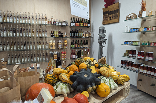 Markttisch mit verschiedenen Kürbissen und Gläsern auf Regalen im Hintergrund, die lokale Produkte präsentieren.