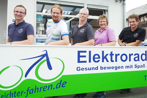 Fünf Personen stehen lächelnd vor einem Geschäft für Elektrofahrräder mit einem großen Schild.