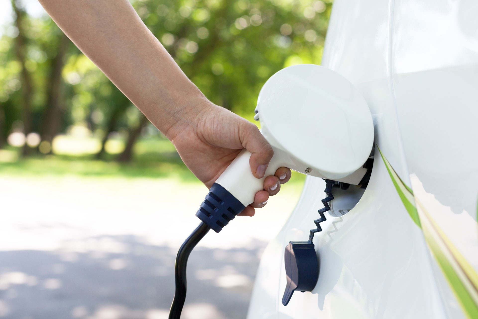 Eine Hand hält einen Ladestecker, der in eine Elektroautoladestation eingesteckt wird, um das Fahrzeug aufzuladen.