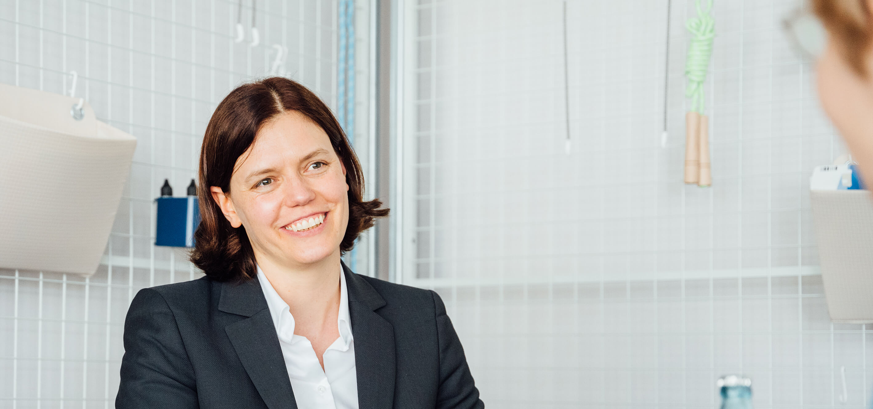 Lächelnde Frau in einem modernen Büro mit Anzug, sitzt an einem Tisch und führt ein Gespräch.