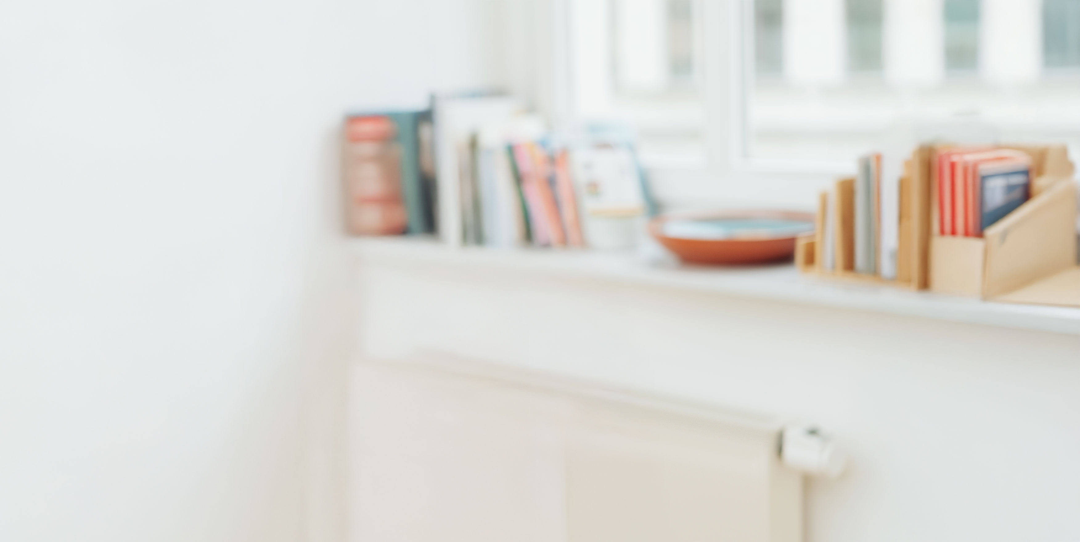 Blick auf ein helles Zimmer mit Bücherregal und Keramikschale auf dem Fensterbrett. Gemüseheizung im Vordergrund.