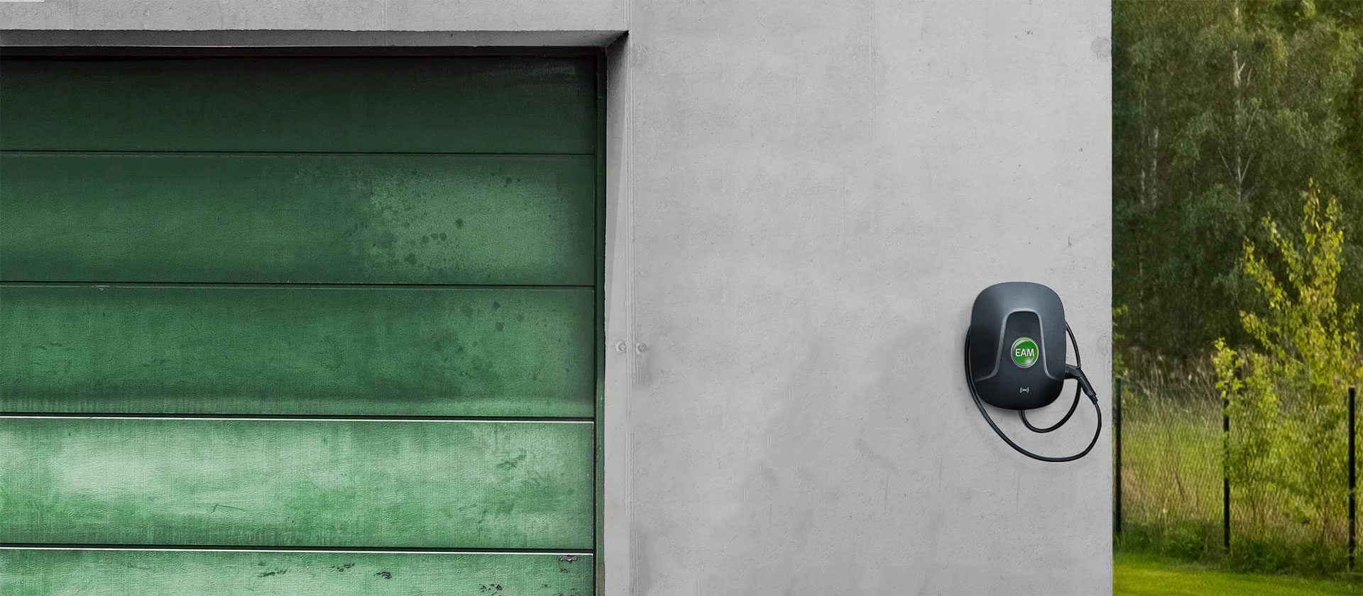 Wandmontierte Ladestation für Elektrofahrzeuge neben einer grünen Garagentür.