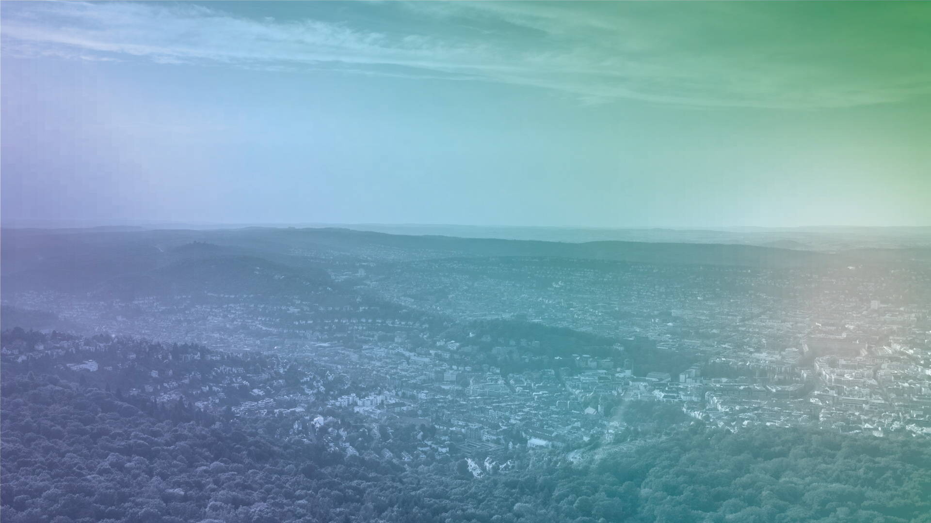 Panoramablick über eine bewaldete Landschaft und eine Stadt im Hintergrund unter einem leicht bewölkten Himmel.