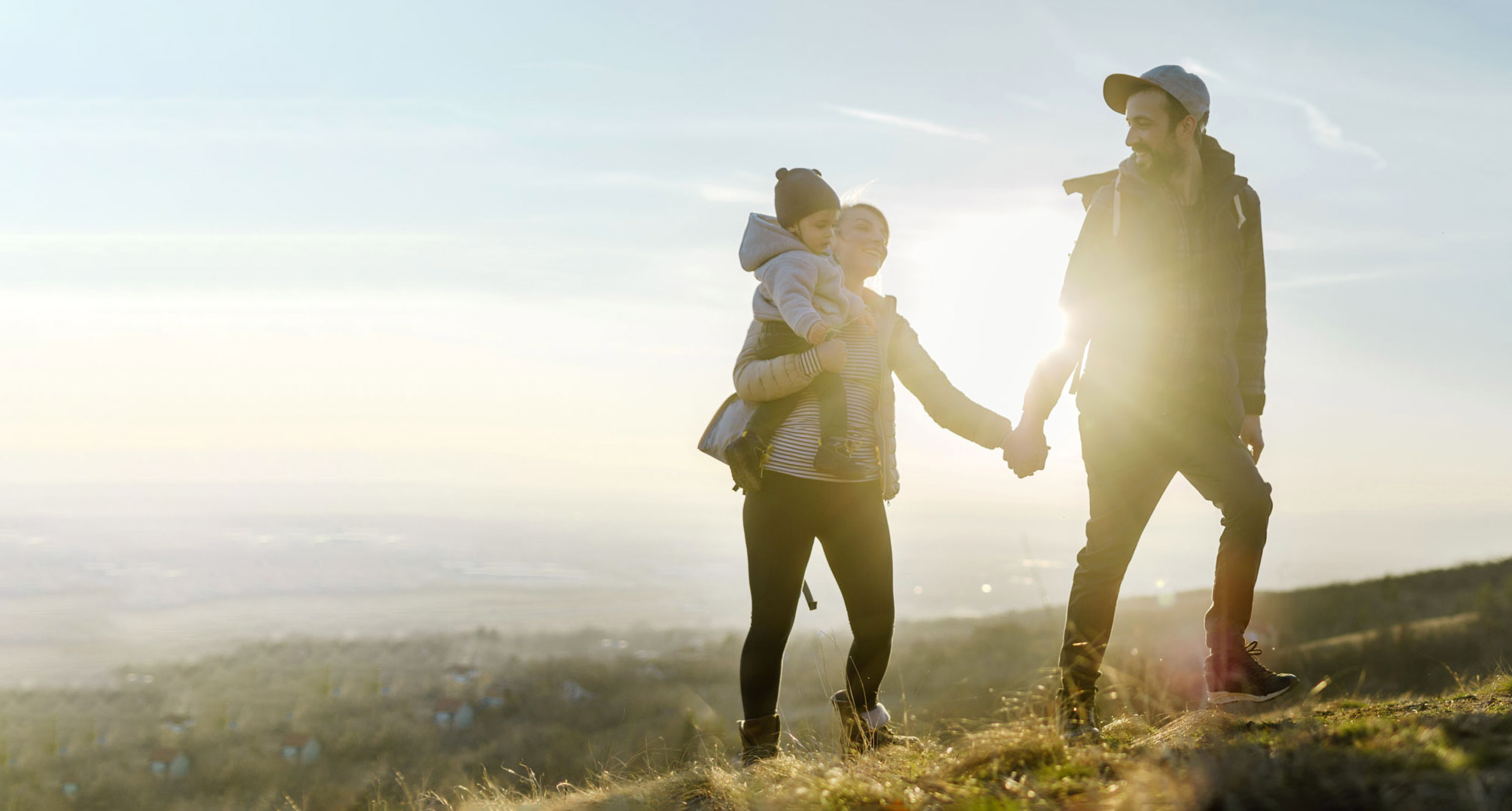Familie beim Spaziergang auf einem Hügel in der Abenddämmerung, die Sonne strahlt im Hintergrund.