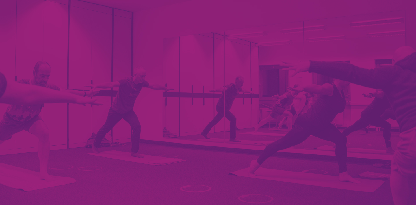 Mehrere Personen in Sportkleidung führen Yogaübungen in einem Spiegelraum aus. Der Raum ist hell erleuchtet.
